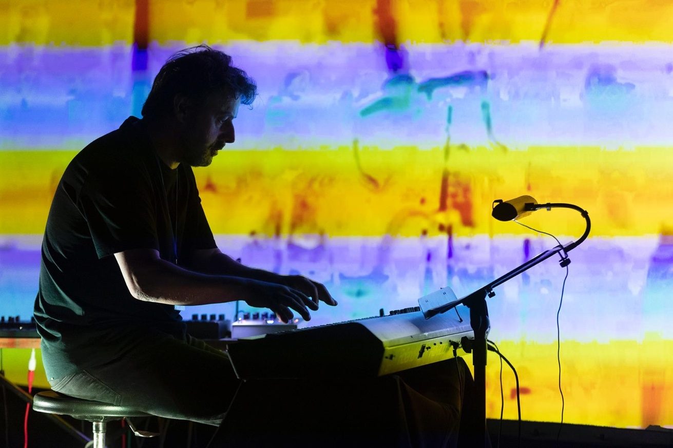 Eamon O'Malley performing 24:09 — silhouetted at the piano against a projected backdrop